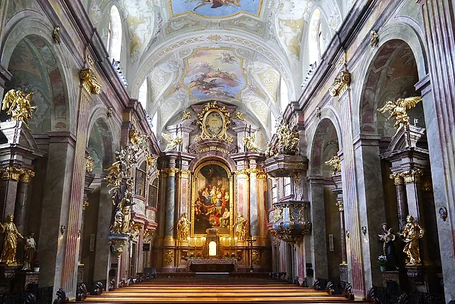 A nave da Annakirche, com pilares marmorizados em tons pastel, estátuas douradas, afrescos no teto e o altar-mor no fim dos bancos vazios