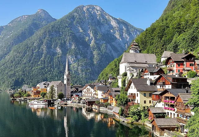 Hallstatt à beira do seu lago, com a esbelta torre da igreja, as casas de madeira ao longo da margem e as montanhas ao fundo, em luz nítida