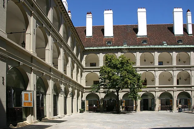 O pátio renascentista de arcadas da Stallburg, na Hofburg de Viena, com seus andares de arcos, as chaminés brancas e uma árvore ao centro, sob um céu azul